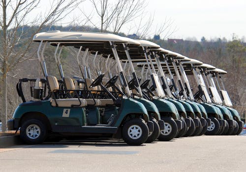 A dozen, green, single seater golf buggies in a row.